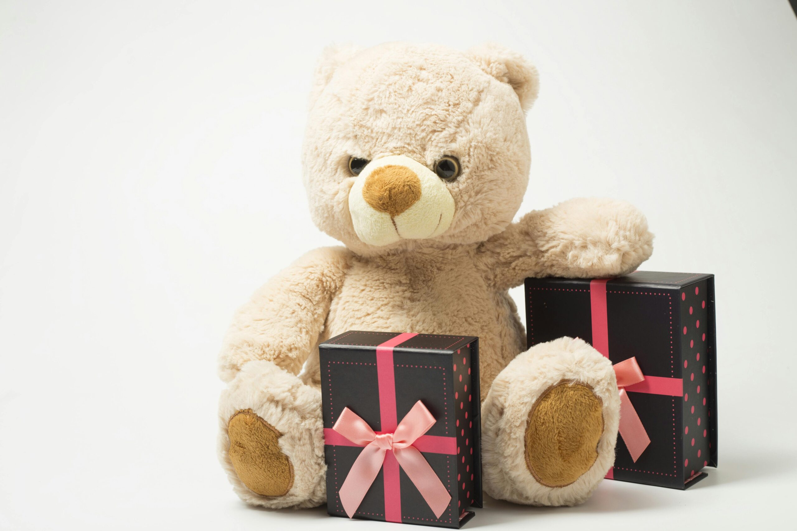 Adorable teddy bear with gift boxes tied with pink ribbons, perfect for celebrations.